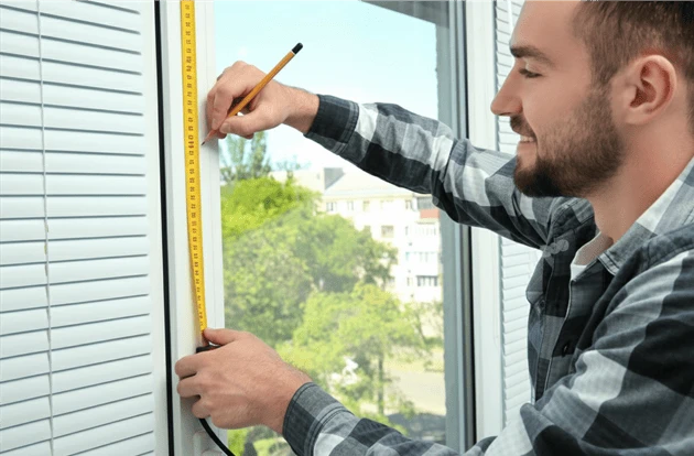 Мастер с рулеткой измеряет пластиковое окно ПВХ 